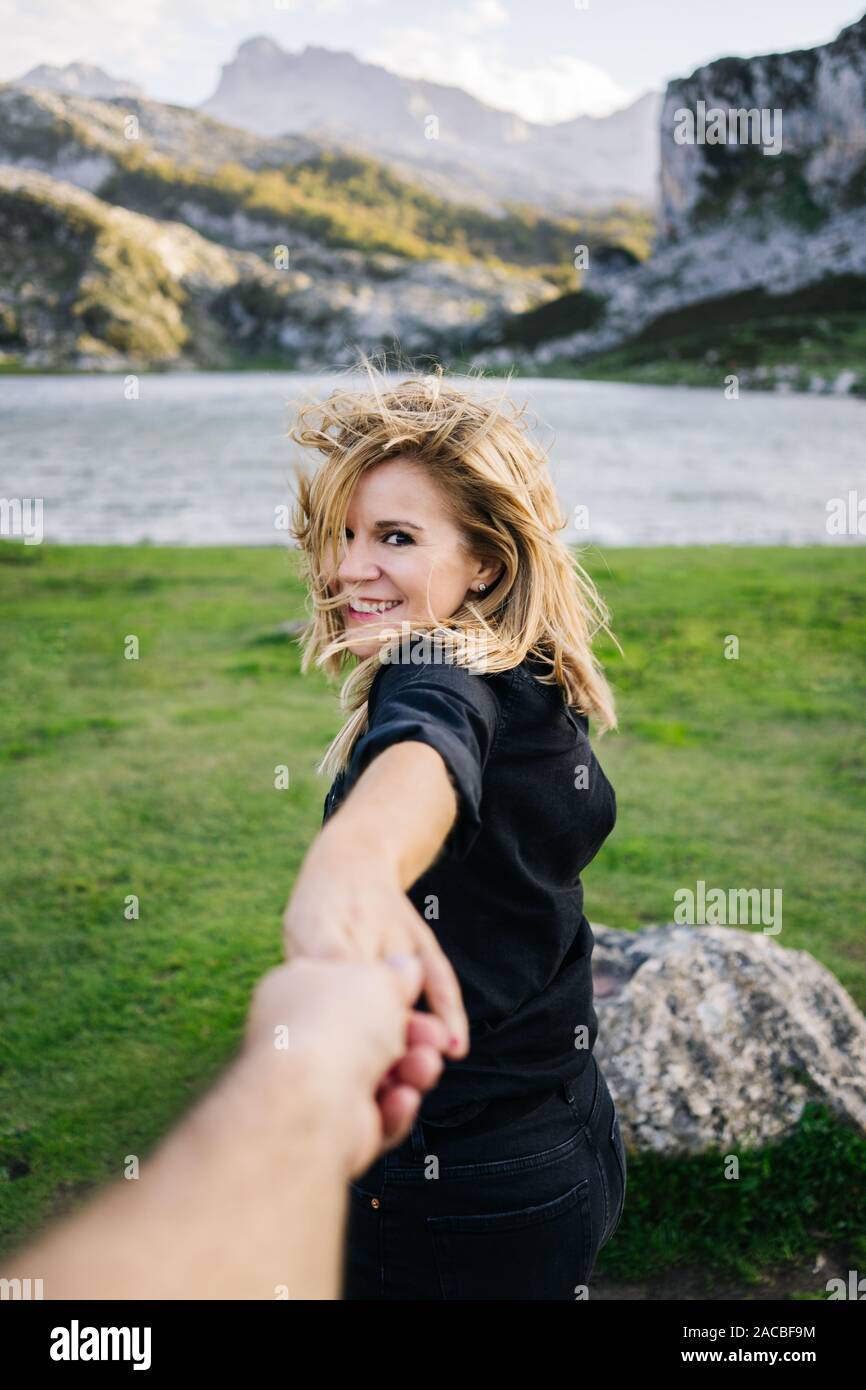 Eine schöne kaukasischen blonde Frau hält die Hand eines Mannes in einer bergigen Landschaft mit See Stockfoto