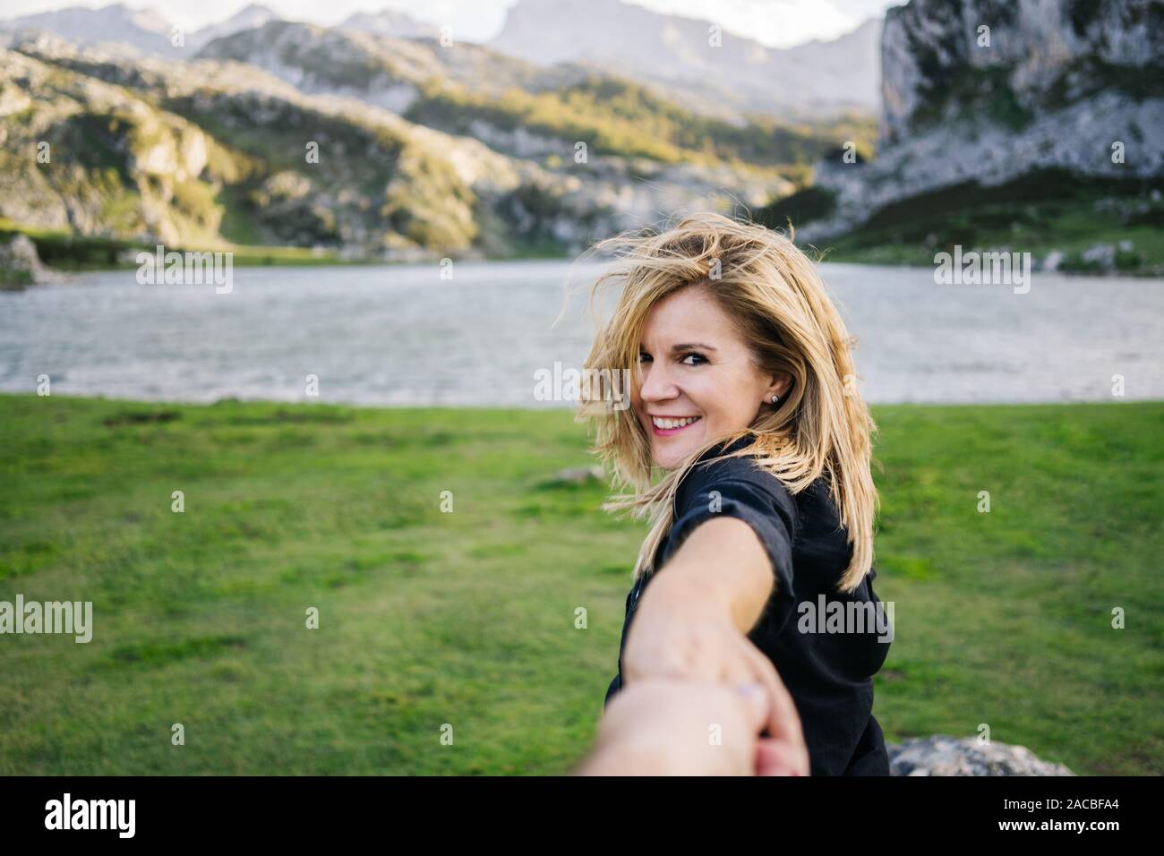 Eine schöne kaukasischen blonde Frau hält die Hand eines Mannes in einer bergigen Landschaft mit See Stockfoto