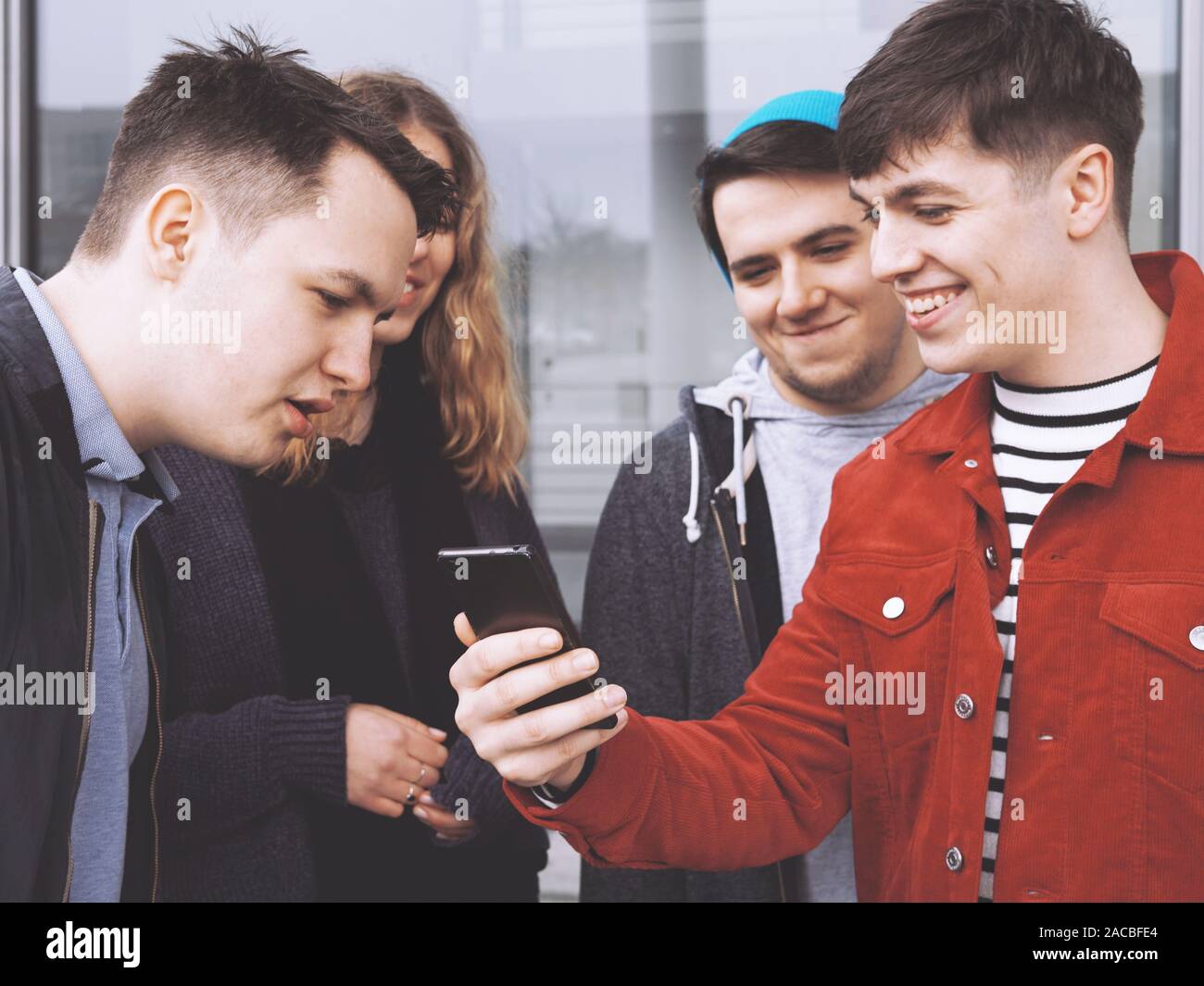 Junger Mann mit etwas Lustiges auf seinem Smartphone zu einer Gruppe von jungen Freunden, den Schwerpunkt auf die Hand, Mobiltelefon, matt Filter Stockfoto