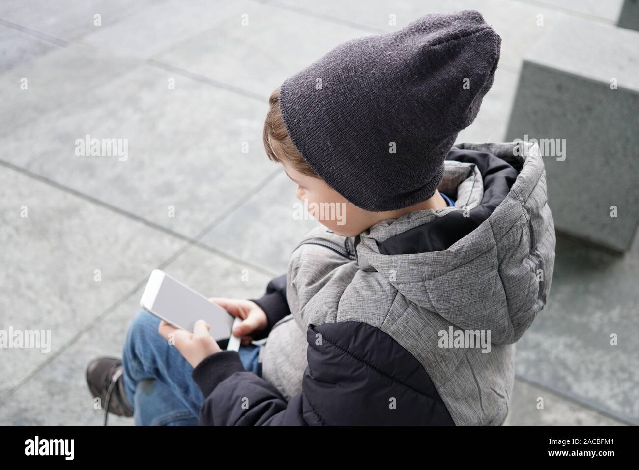 7 Jahre alten Jungen auf Smartphone Handy draußen auf der Straße im Winter Stockfoto