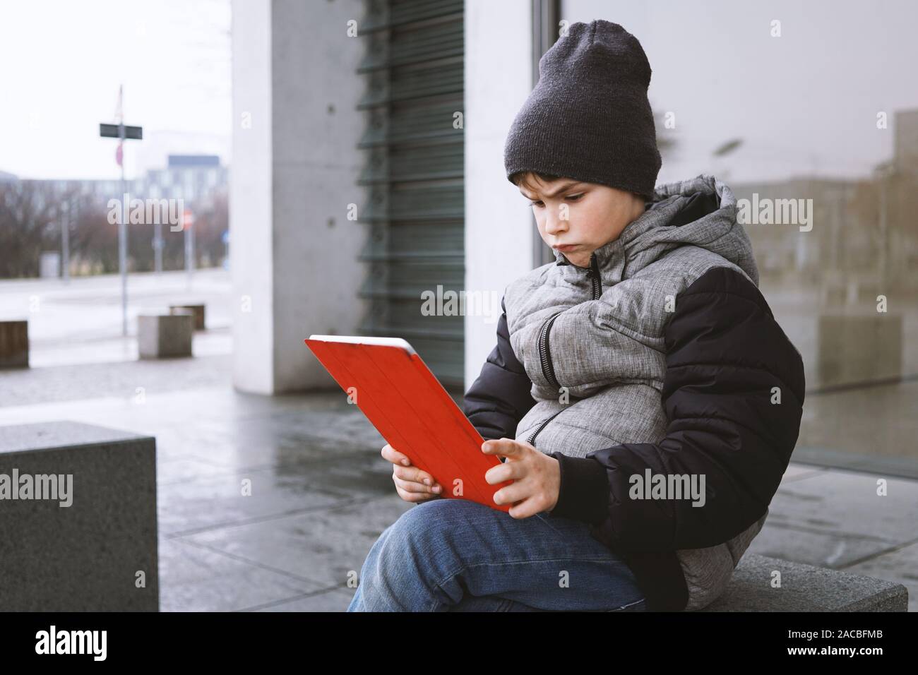 Junge Junge an Tablet PC-Computer mit frustrierten Blick auf seinem Gesicht während draußen sitzen nur auf der Straße im Winter Stockfoto