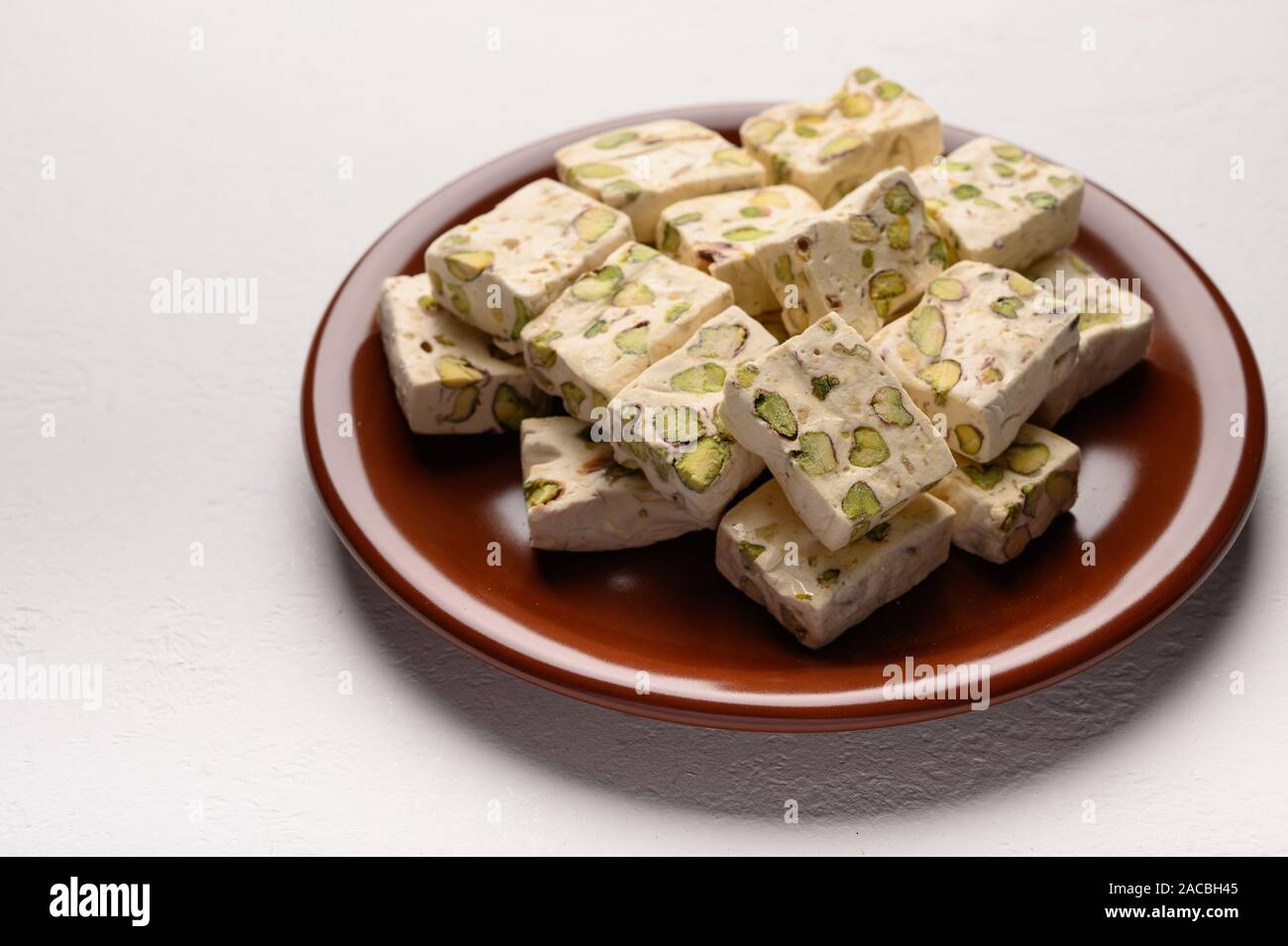 Osten Arabisch nougat Süße mit Pistazien auf einem braunen Keramikplatte auf einem hellen Hintergrund Stockfoto