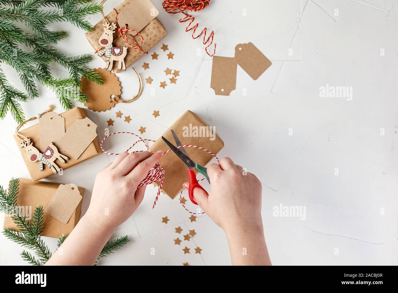 Die Frau Hände wickeln Weihnachten handgefertigt in Papier mit Garn- und Weihnachtsdekorationen und Tannenzweigen. DIY Hobby. Ansicht von oben mit der Kopie Raum Stockfoto