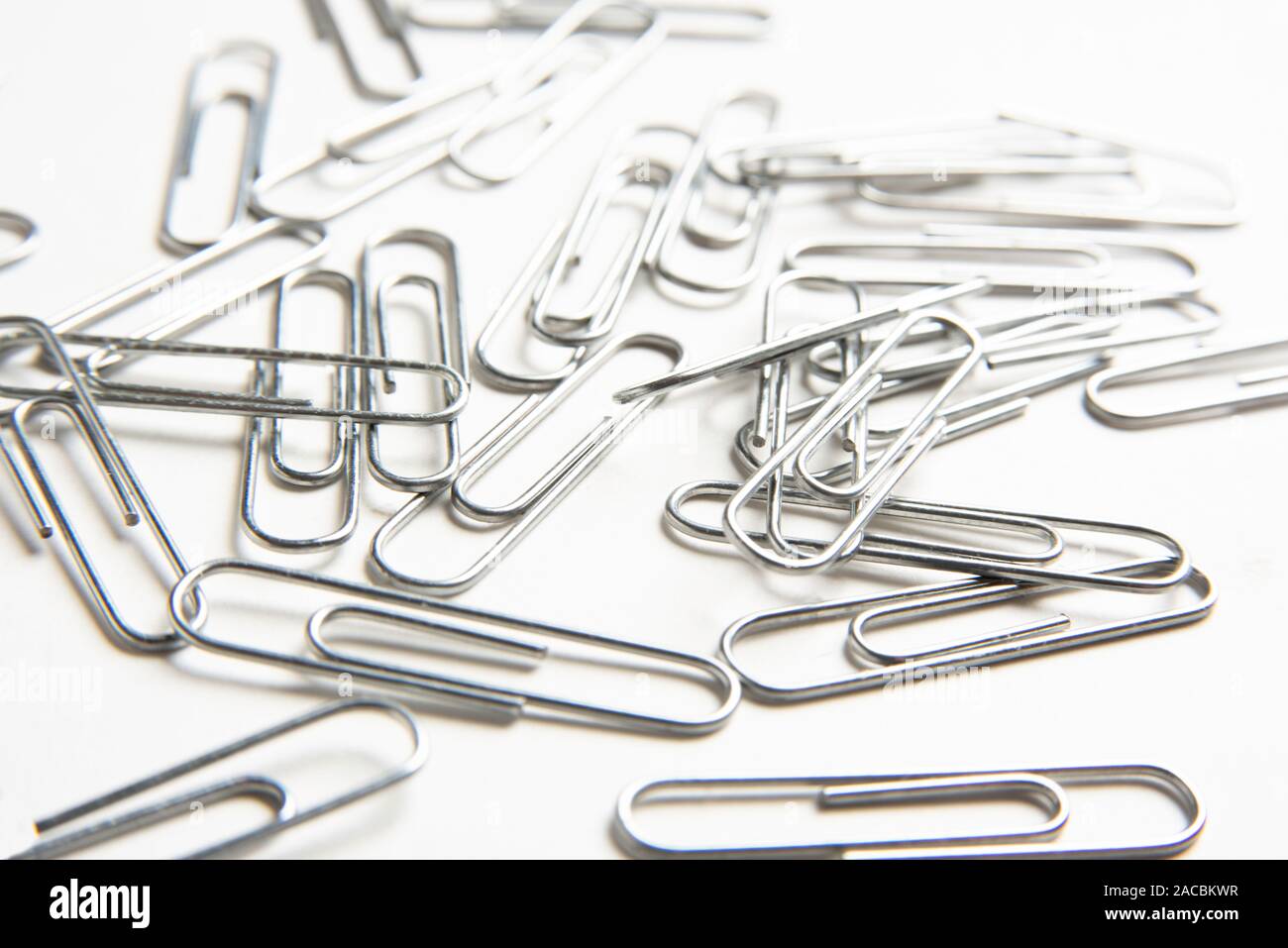 Ein Bündel von silberfarben Metall Büroklammern auf einem schlichten weißen Hintergrund verstreut. Stockfoto