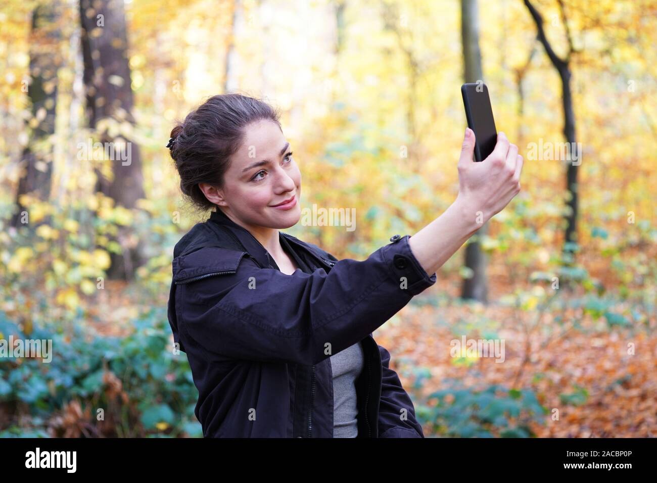 Junge Frau in ihrem 20s, selfie Selbstportrait mit Ihrem Smartphone Mobiltelefon im Herbst Spaziergang im Wald Stockfoto