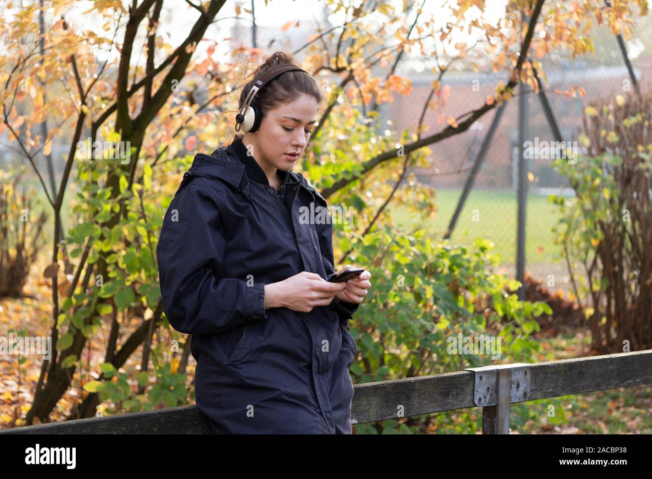 Junge Frau in ihrem 20s Abspielen von Musik mit drahtlosen Bluetooth® Kopfhörer und smart phone - candid urbanen Lebensstil im Freien im Herbst - mit Kopie Raum Stockfoto