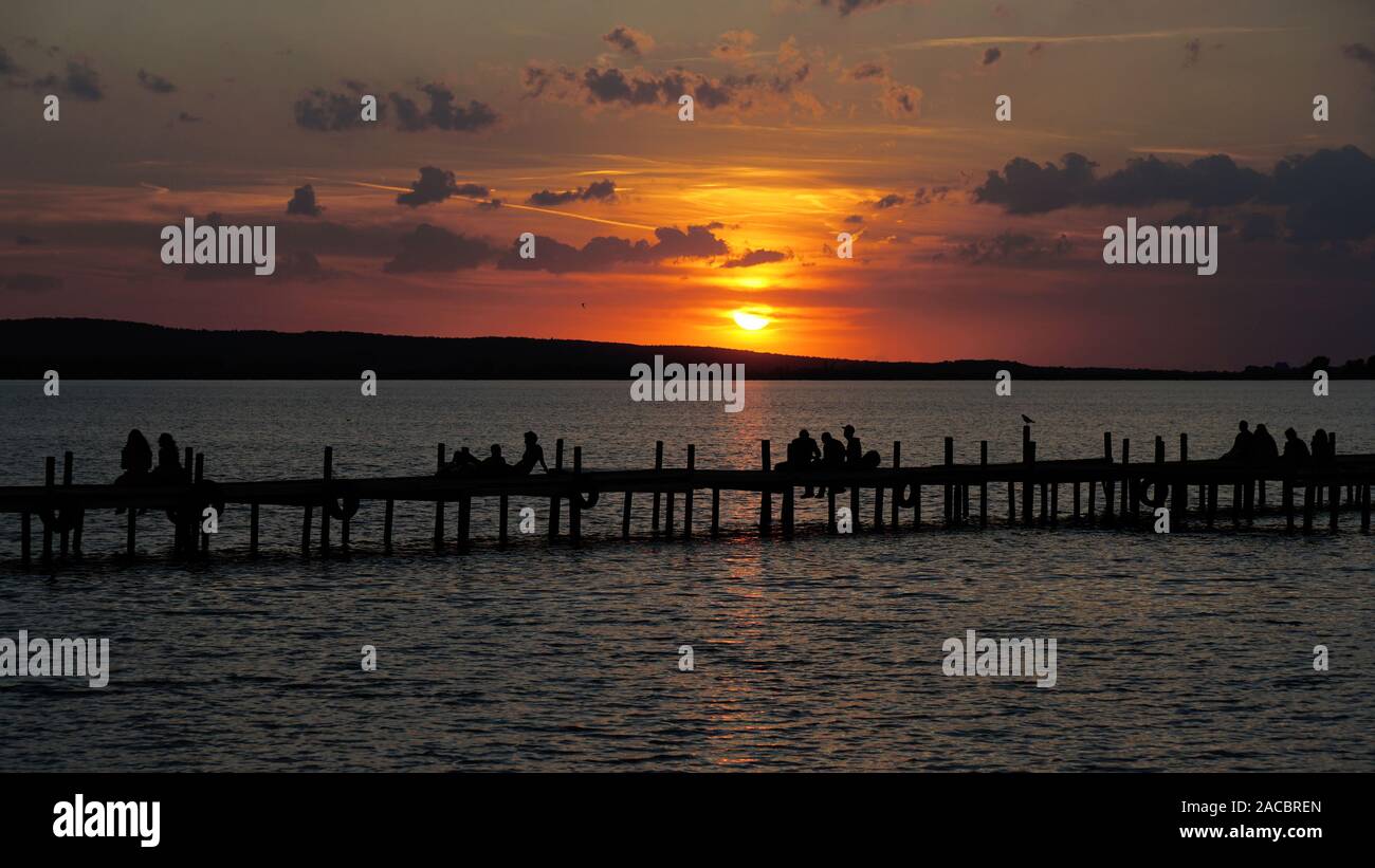 Gruppe von Personen unkenntlich in Silhouette sitzen auf Jetty Pier beobachten Sonnenuntergang Sonnenuntergang am See Steinhuder Meer in Deutschland Stockfoto