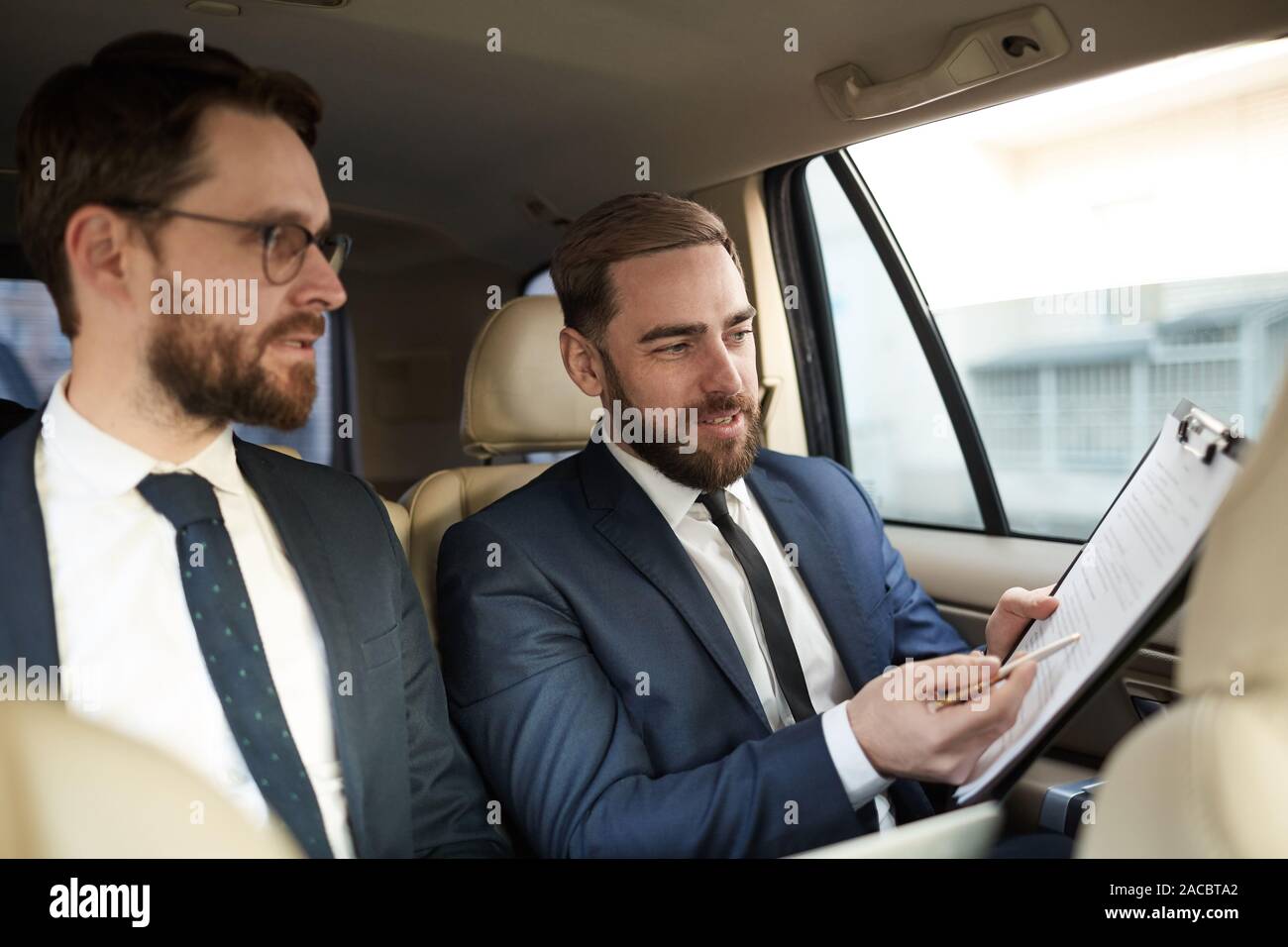 Junge Unternehmer, die an den Vertrag und diskutieren es mit seinem Kollegen, während Sie sitzen auf der Rückbank des Autos Stockfoto