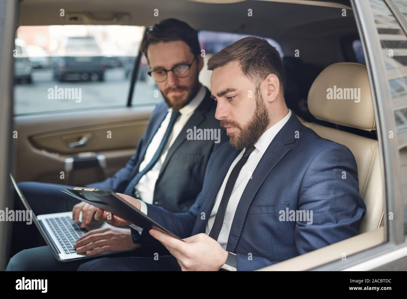 Zwei Geschäftspartnern mit Laptop und diskutieren Dokument zusammen auf der Rückseite des Sitzes während der Fahrt Stockfoto