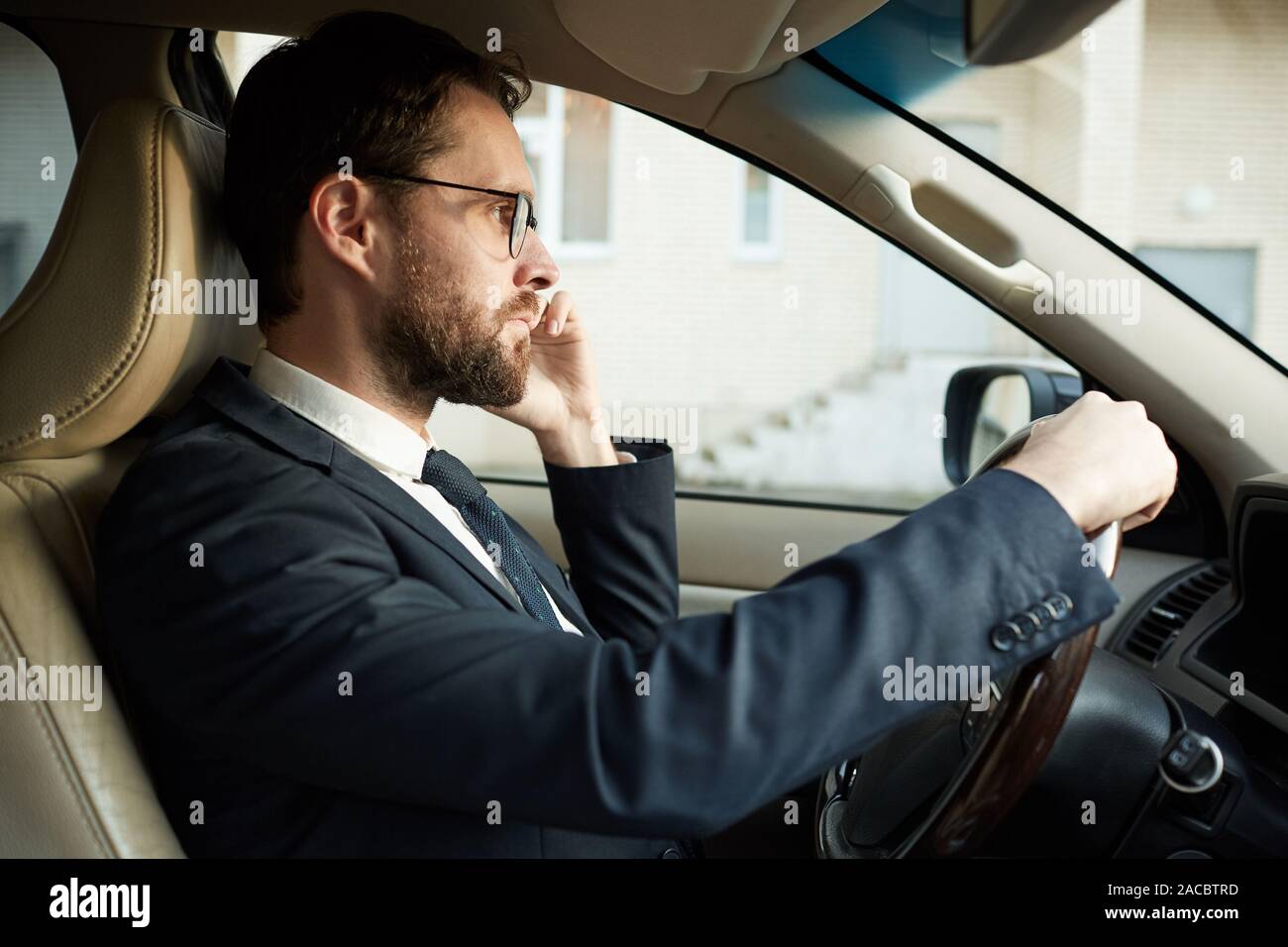 Seitenansicht des eleganten Fahrer im Gespräch am Handy und auf der Straße, während das Auto fahren Stockfoto