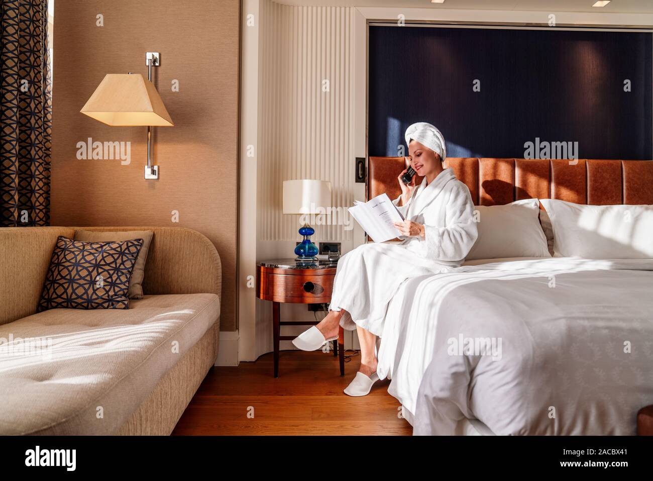 Hübsche junge Frau sprechen, die auf dem Handy in ihr Bett und Lesen. Stockfoto