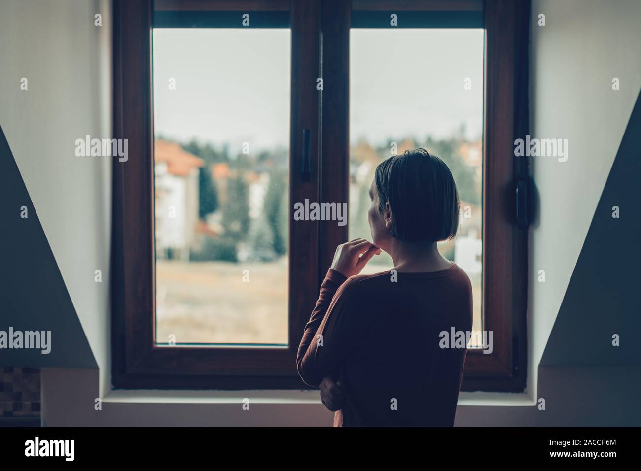 Traurige Frau schaut aus dem Fenster in loft apartment Stockfoto