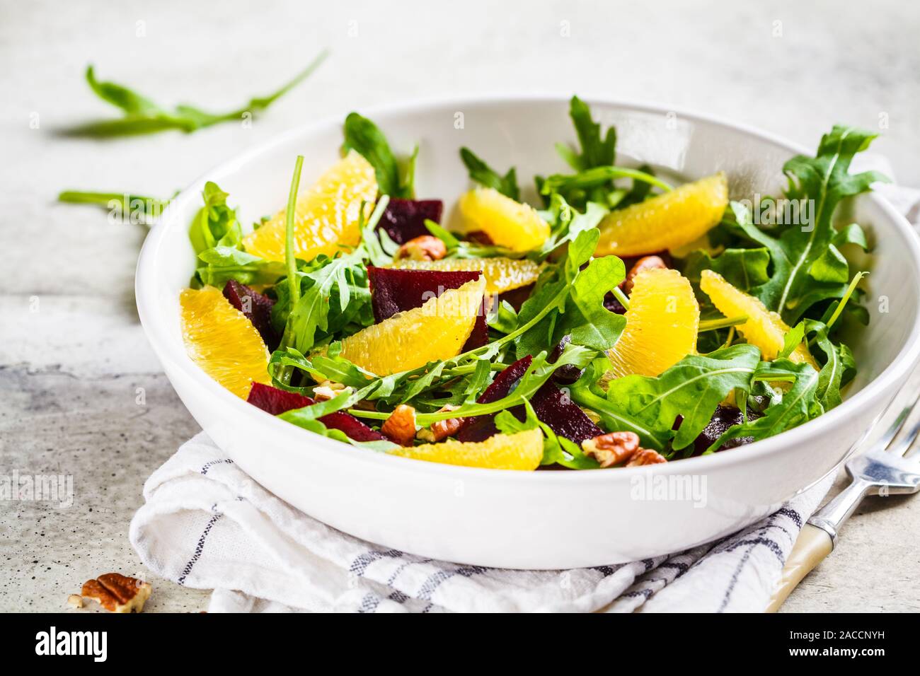 Zuckerrüben- und orange-Salat mit Rucola und Nüsse in einer weißen Schüssel. Gesunde vegane Ernährung Konzept. Stockfoto