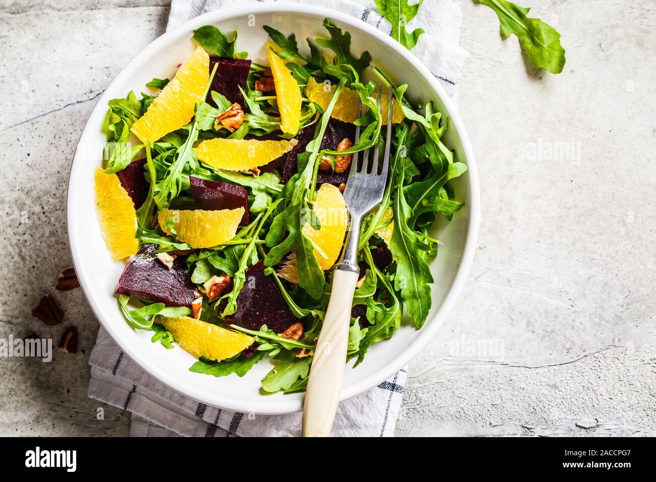Zuckerrüben- und orange-Salat mit Rucola und Nüsse in einer weißen Schüssel. Gesunde vegane Ernährung Konzept. Stockfoto