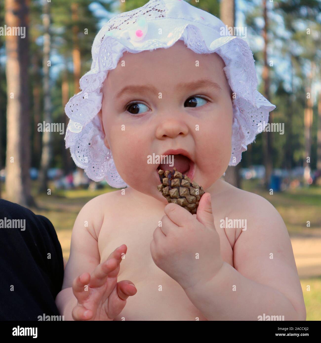 Adorable Baby Mädchen in eine Kappe mit Rüschen spielen mit Pine Cone im Freien gekleidet Stockfoto