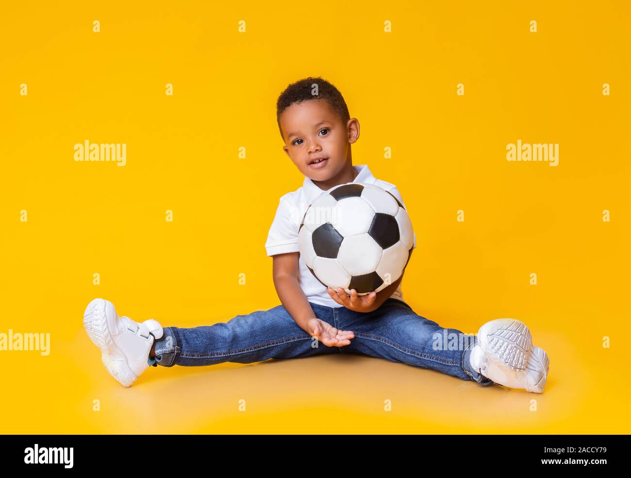 Adorable afro baby boy mit Fußball sitzen auf dem Boden Stockfoto