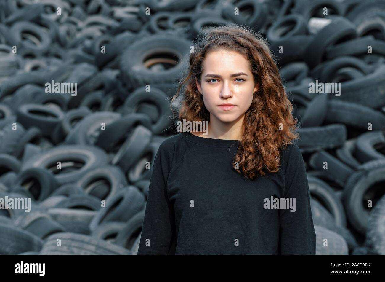 Schöne Mädchen, lockiges Haar, Porträt vor dem Hintergrund der einen Dump der alten Autoreifen. Mit Blick auf die Kamera. Stockfoto