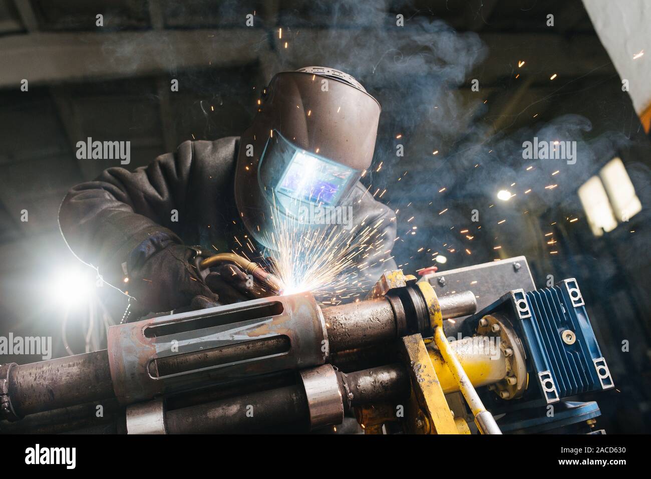 Schweißer bei der Arbeit abgedeckt. Er ist Schweißen metall Stück, mit industriellen Schelle befestigt. Stockfoto