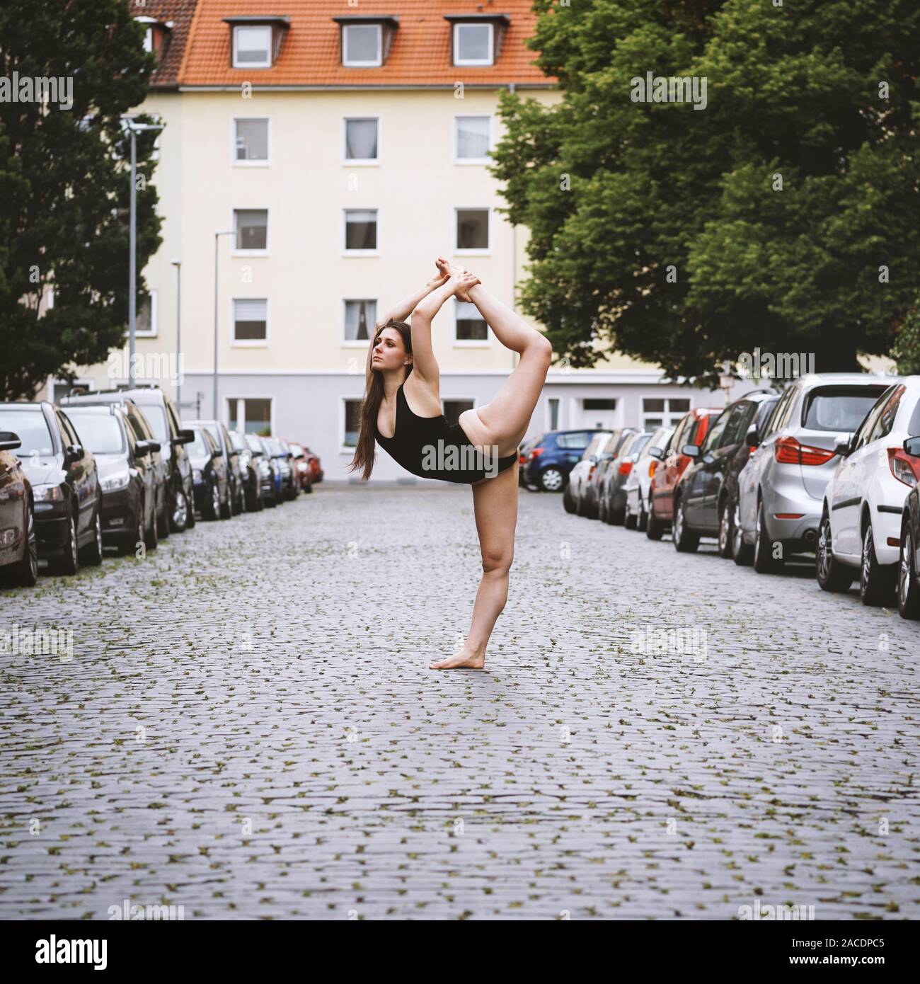 Unbeschwerte junge Frau Ballet Dancer Ausübung auf Straße der Stadt - städtische Ballerina tragen leotard zeigt Flexibilität und Lebendigkeit in Yoga pose Stockfoto
