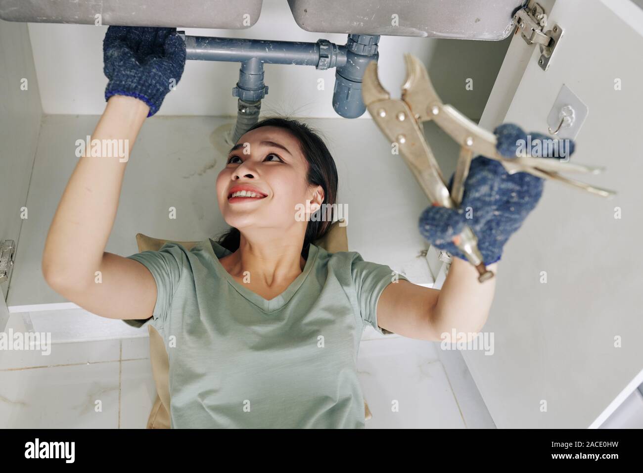 Fröhliche junge Frau Schutzhandschuhe bei der Festsetzung tropfende Spüle Rohr in der Küche Stockfoto