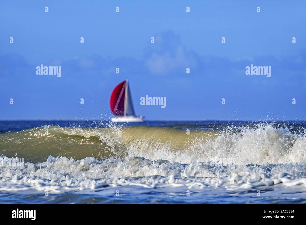 Wellen brechen am Strand und Segelboot/Segelboot mit roten Segeln auf See Stockfoto