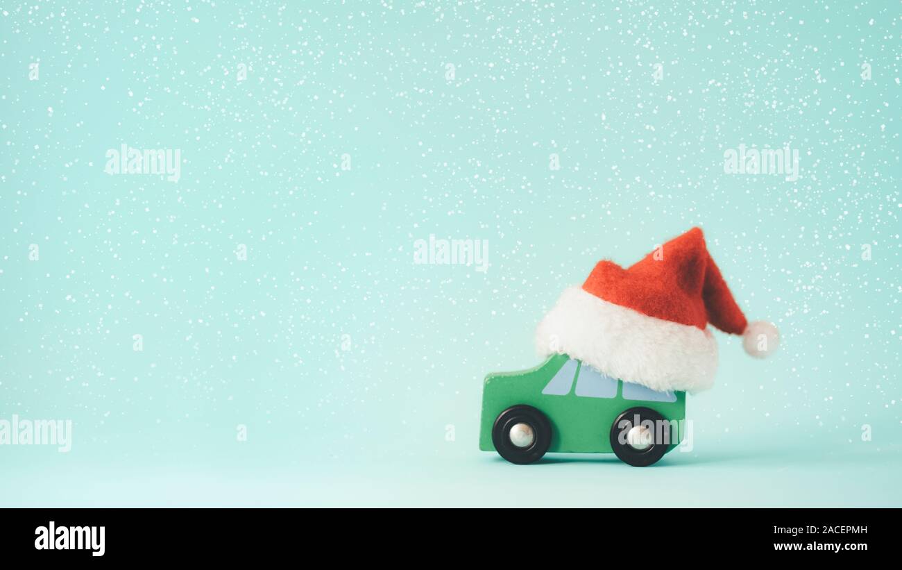 weihnachten oder Neujahr minimaler Kopierraum Hintergrund. Das hölzerne Spielzeugauto und der Weihnachtsmann Hut auf Schnee und mintfarbenen Hintergrund. Stockfoto