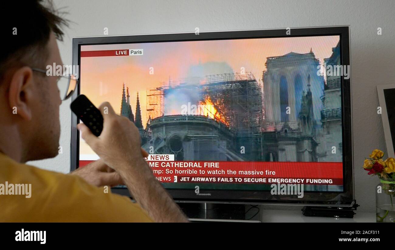 Paris, Frankreich, 15. April 2019: Mann mit Fernbedienung auf den Fernseher im Wohnzimmer, die letzten Nachrichten mit der britischen BBC World News Channel Live broadcast aus der Notre-Dame de Paris Feuer suchen Stockfoto