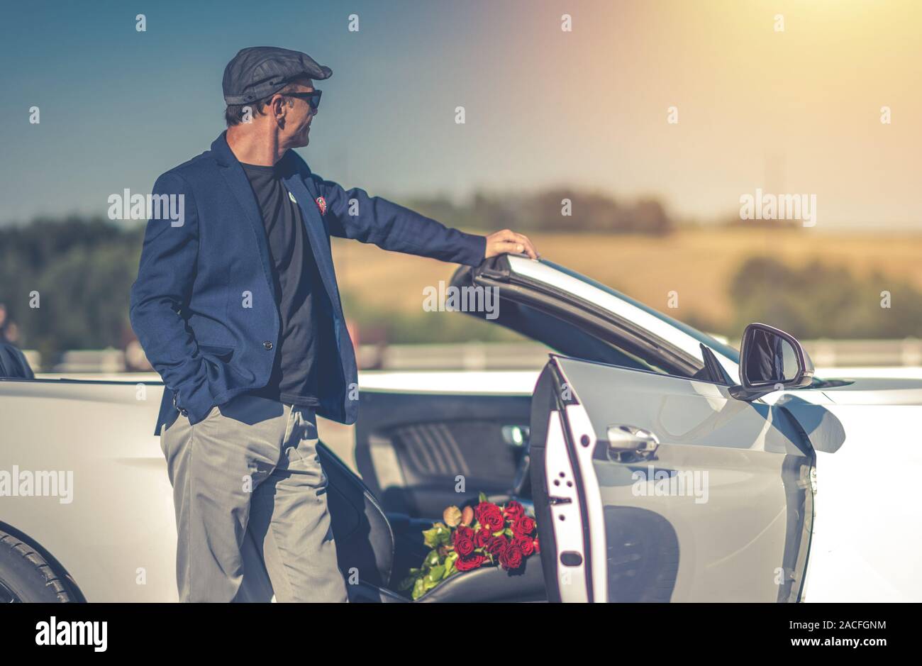 Elegante romantische Männer in seinem 60s Klicken Sie auf ein Datum mit roten Rosen Blumenstrauß in seinem Cabrio. Stockfoto