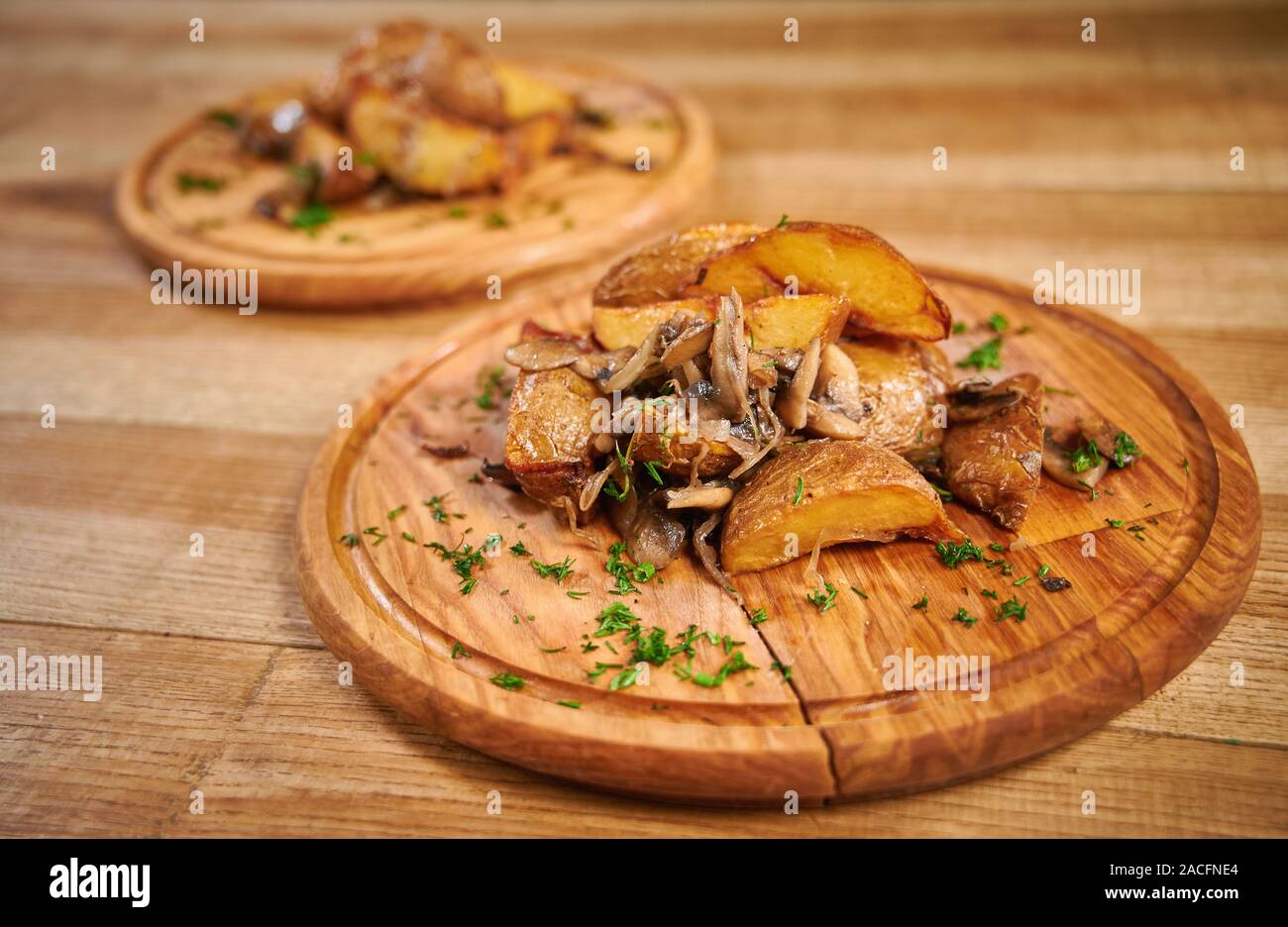 Gebratene Kartoffeln mit Pilzen. Holzbrett mit leckeren Kartoffelecken mit Pilzen auf Tisch Stockfoto