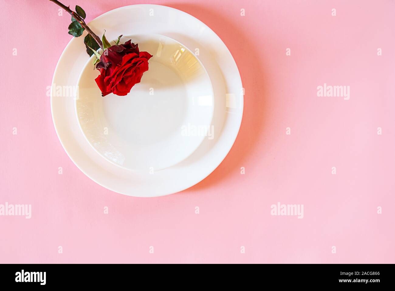 Romantisch gedeckten Tisch für Valentines Tag oder Abendessen Datum Feier Hochzeit. Valentines Tag Konzept mit rote Rose Bud White Platten auf Pastell rosa Tischdecke Hintergrund. Flach, Ansicht von oben kopieren. Stockfoto