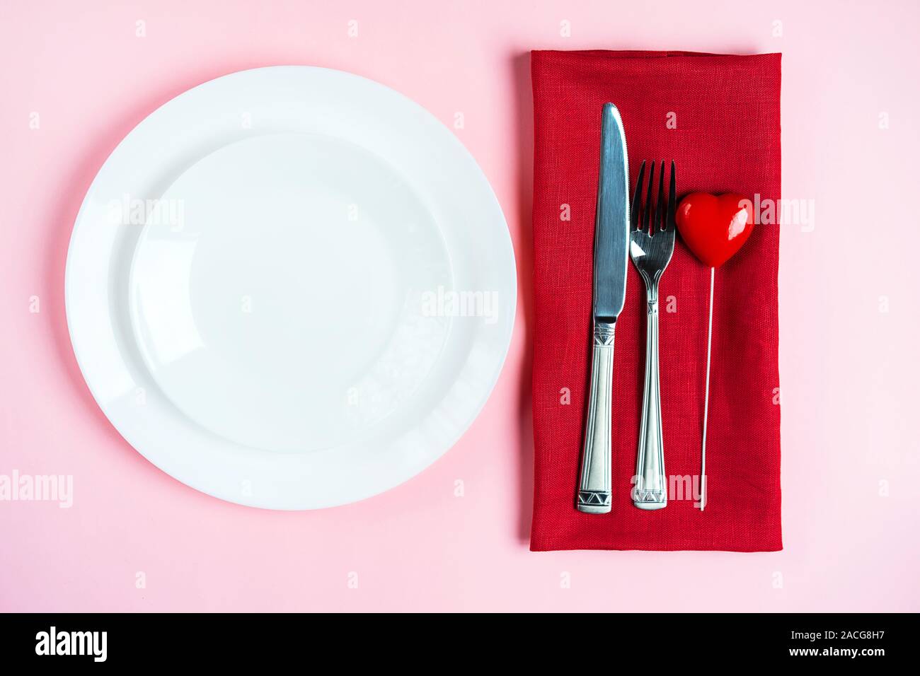 Festliche Tischdekoration für den Valentinstag mit Gabel, Messer und Herzen auf rosa Tabelle Hintergrund. Platz für Text. Ansicht von oben, flach. Stockfoto