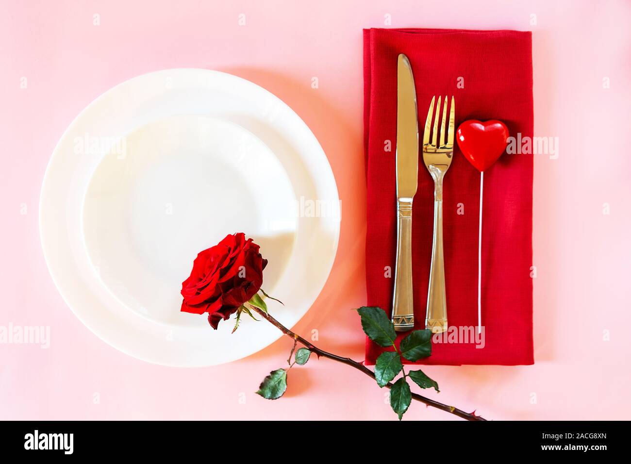 Romantisch gedeckten Tisch für Valentines Tag oder Abendessen Datum Feier Hochzeit. Valentines Tag Konzept mit rote Rose Bud White Platten auf Pastell rosa Tischdecke Hintergrund. Flach, Ansicht von oben kopieren. Stockfoto