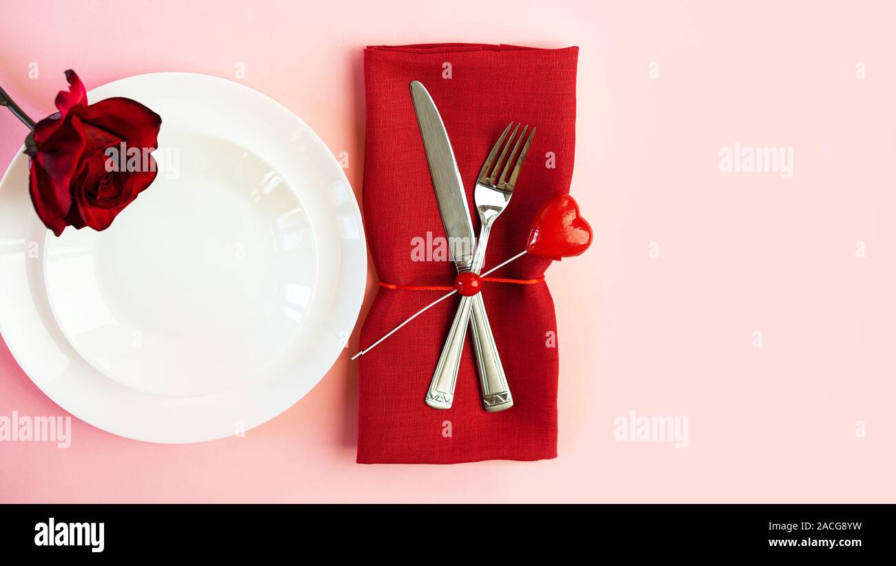 Romantisch gedeckten Tisch für Valentines Tag oder Abendessen Datum Feier Hochzeit. Valentines Tag Konzept mit rote Rose Bud White Platten auf Pastell rosa Tischdecke Hintergrund. Flach, Ansicht von oben kopieren. Stockfoto