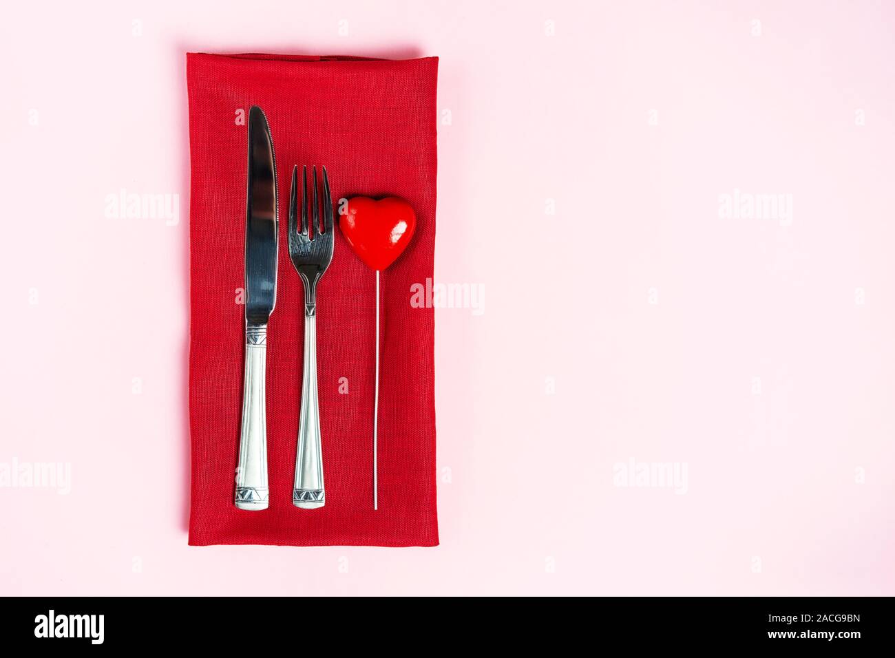 Festliche Tischdekoration für den Valentinstag mit Gabel, Messer und Herzen auf rosa Tabelle Hintergrund. Platz für Text. Ansicht von oben, flach. Stockfoto