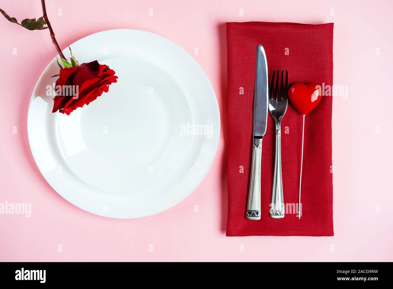 Romantisch gedeckten Tisch für Valentines Tag oder Abendessen Datum Feier Hochzeit. Valentines Tag Konzept mit rote Rose Bud White Platten auf Pastell rosa Tischdecke Hintergrund. Flach, Ansicht von oben kopieren. Stockfoto