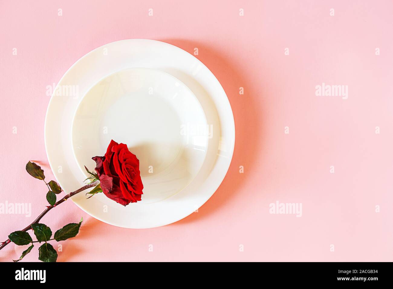 Romantisch gedeckten Tisch für Valentines Tag oder Abendessen Datum Feier Hochzeit. Valentines Tag Konzept mit rote Rose Bud White Platten auf Pastell rosa Tischdecke Hintergrund. Flach, Ansicht von oben kopieren. Stockfoto