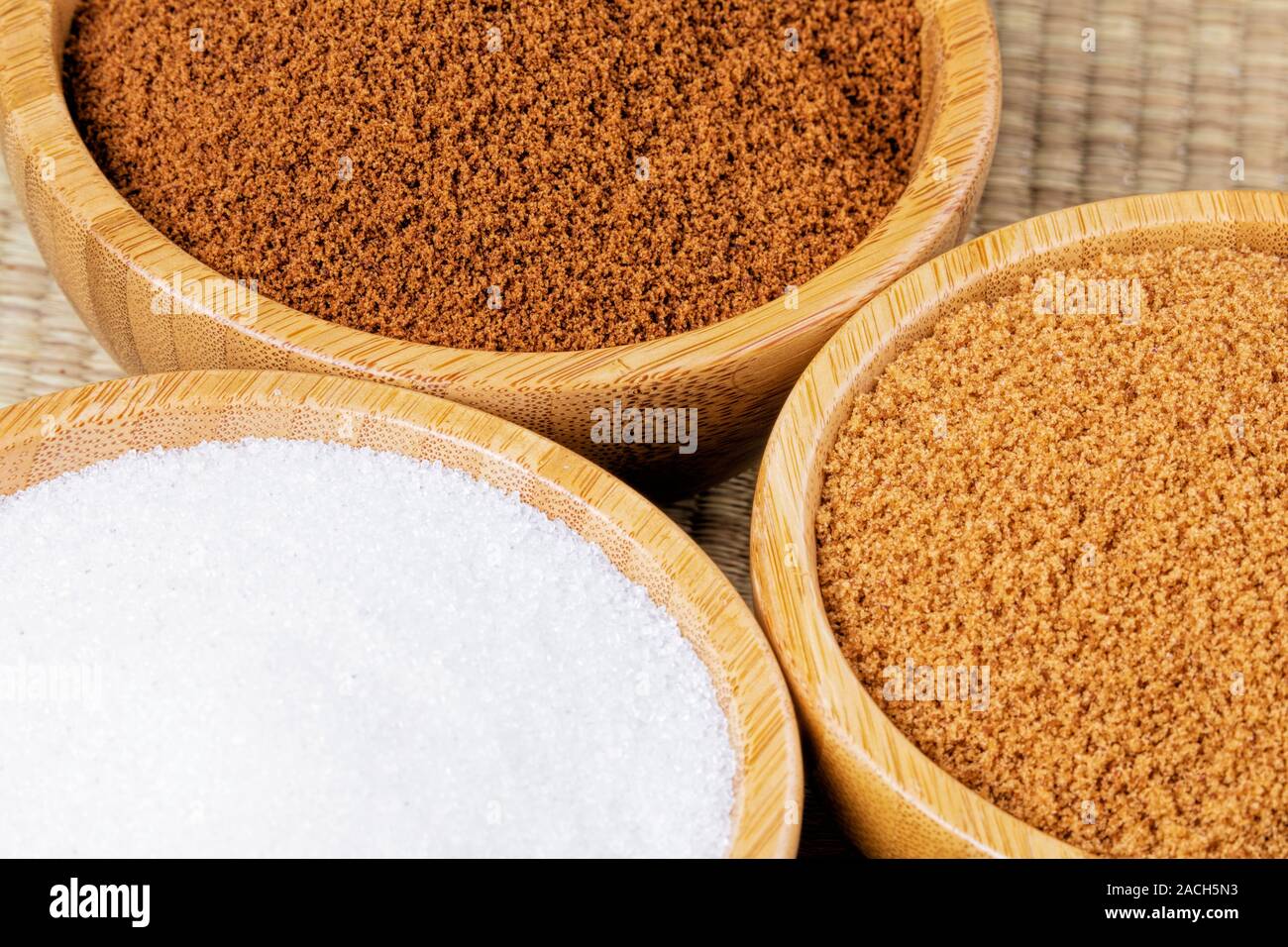 Drei hölzerne Schalen verschiedener Zucker, brauner Zucker, Braun Zucker, und Kristallzucker auf einem Bambus Hintergrund Stockfoto
