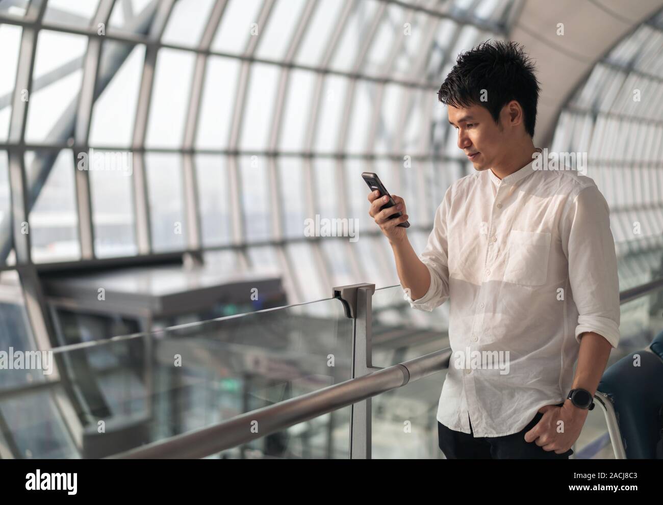 Junger Mann warten auf Flug- und mittels Smart Phone in Flughafen Stockfoto