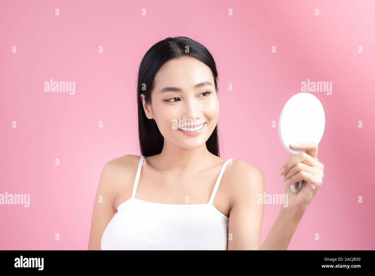 Junge schöne asiatische Frau im Spiegel über rosa Hintergrund suchen Stockfoto