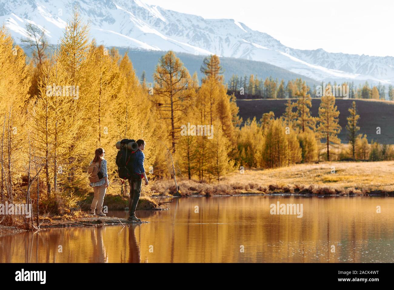 Paar junge Wanderer steht mit Rucksäcken in der Nähe von Mountain Lake und gelben Wald Stockfoto