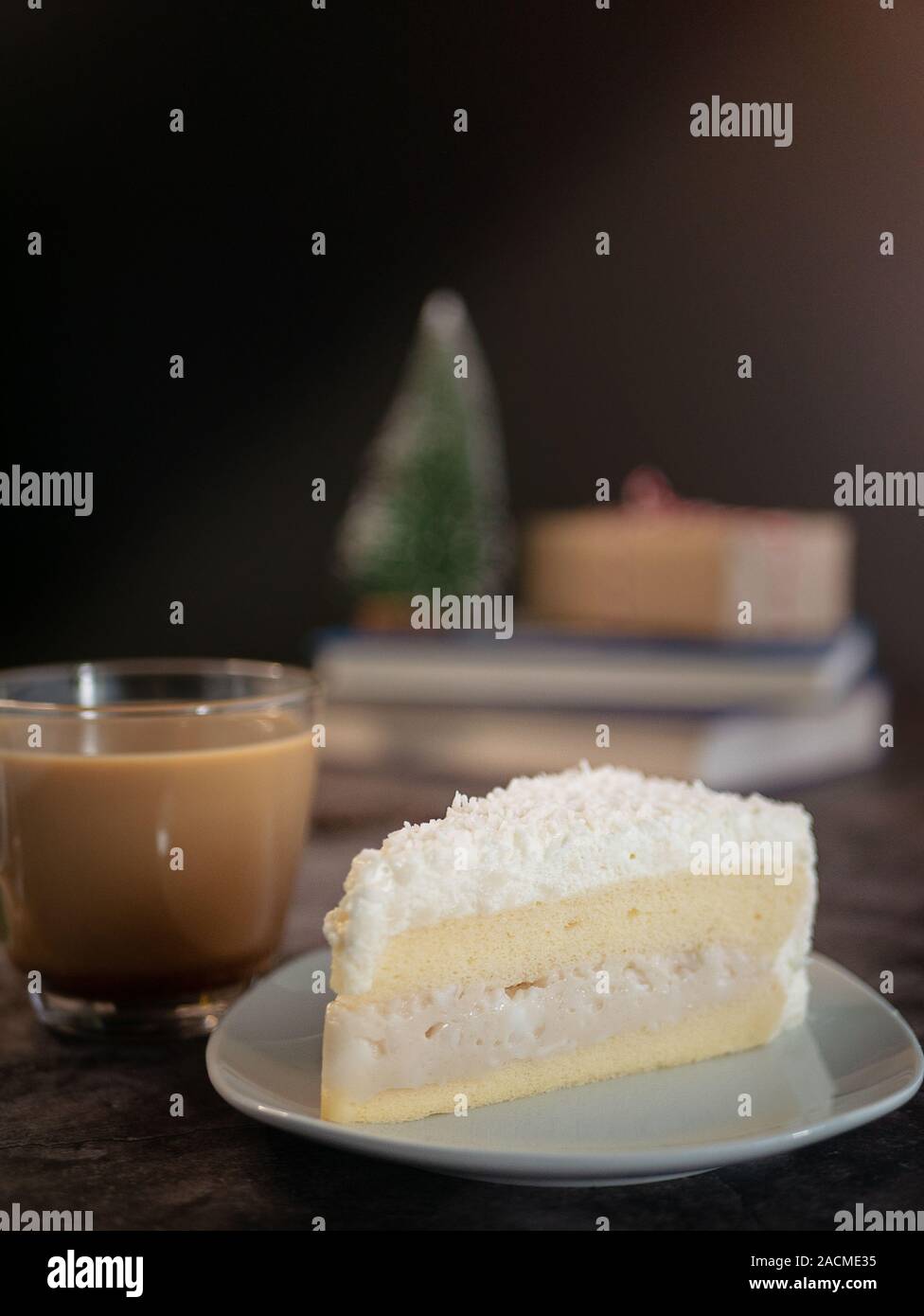 Weiße Schokolade Kuchen mit Kokosnuss Creme Füllung auf weiße Platte mit einer Tasse Kaffee auf den Tisch serviert. vertikale Bild 7/8 Shot Stockfoto