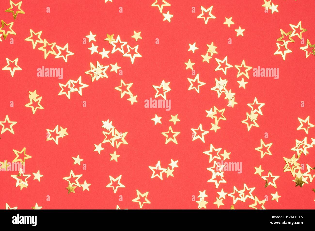 Goldene Sterne Weihnachten Hintergrund auf helles Rot, flatlay, selektiver Fokus Stockfoto