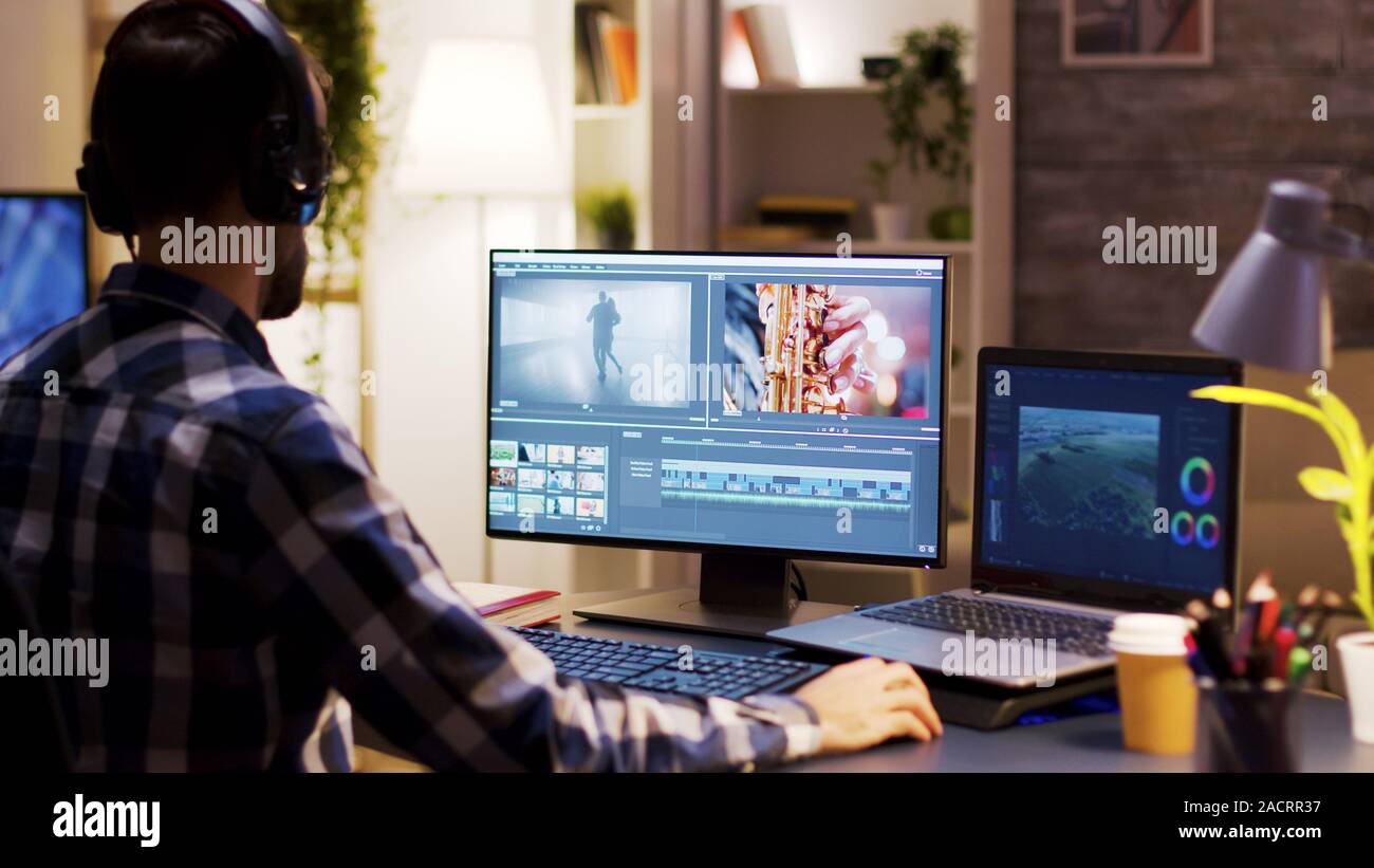 Film Maker zeigt auf den Monitor im Büro zu Hause, während der Arbeit an der Postproduktion für einen Film. Video Editor Kopfhörer tragen. Stockfoto