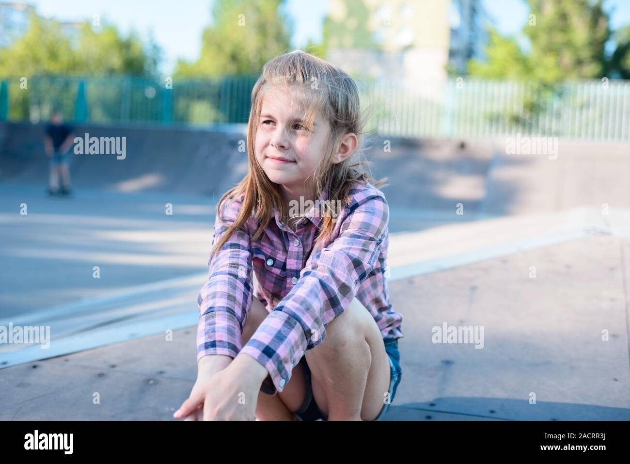 Wenig junges Mädchen, Schülerin sitzt auf einem Skateboard, Sport Park, in einem Plaid Shirt, glücklich, lächeln Stockfoto