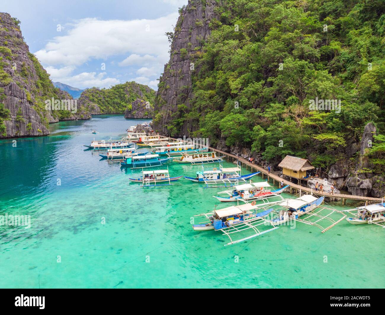 Blue Crystal Wasser im Paradies Bucht mit Booten auf dem Holzsteg am See Kayangan Insel in Coron, Palawan, Philippinen. Stockfoto