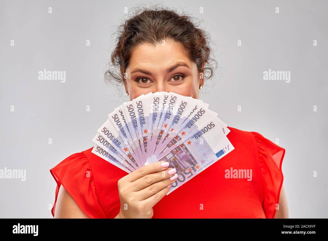 Menschen und Finanzen Konzept - glückliche Frau im roten Kleid ihr Gesicht verstecken hinter Euro Banknoten über grauer Hintergrund Stockfoto
