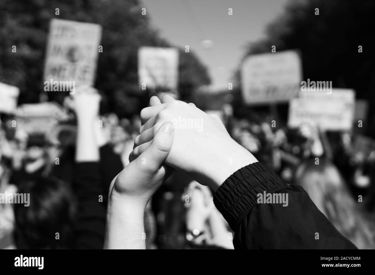 Zwei junge Menschen bei einer Kundgebung, zusammen Hand in Hand Signalisierung Frieden, Einheit und Entschlossenheit vor einer Masse, die Protest Plakate Stockfoto