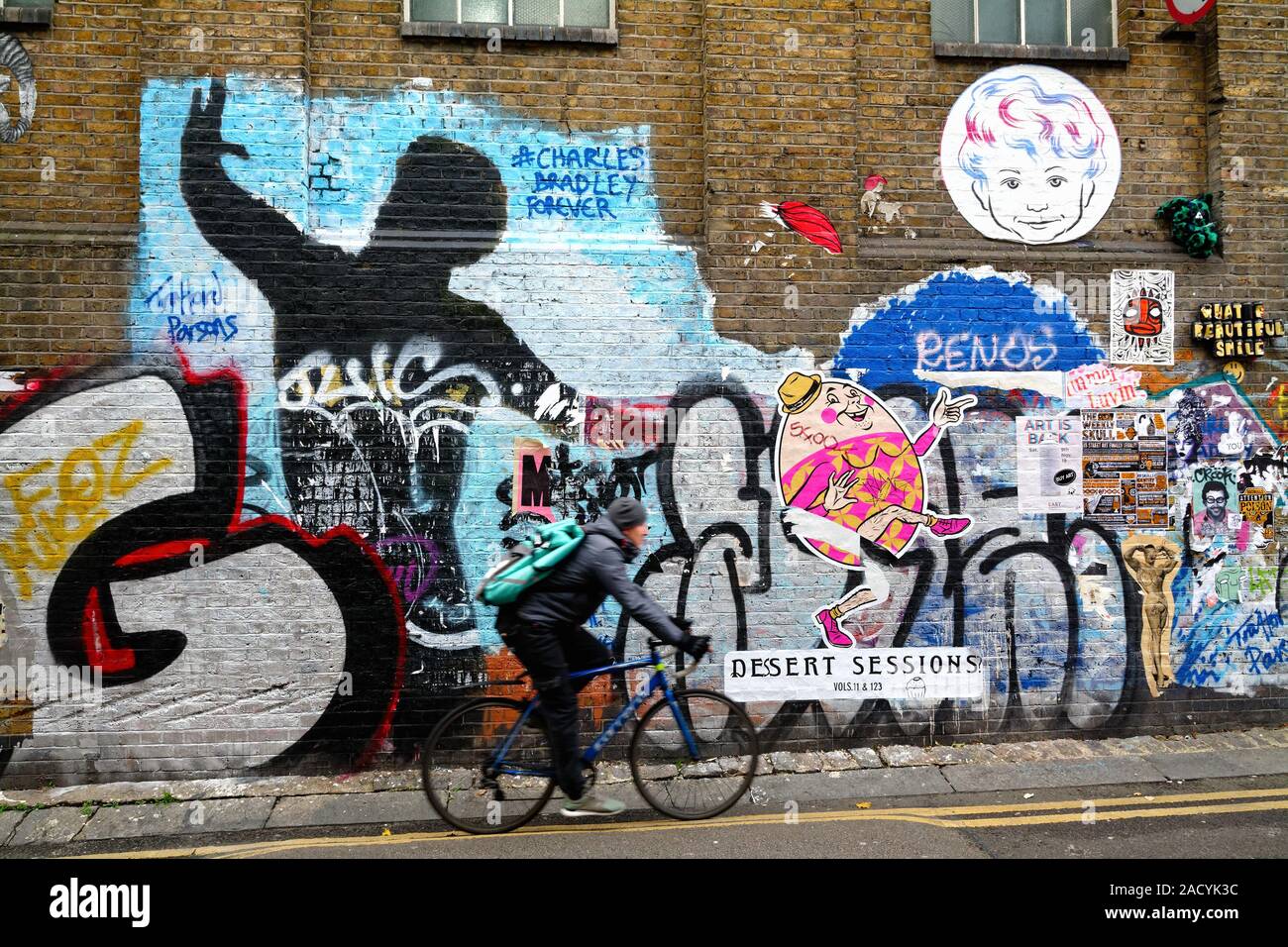 Ein Radfahrer vorbei Graffiti an einer Mauer im Buxton Street off Brick Lane Whitechapel London England Großbritannien Stockfoto