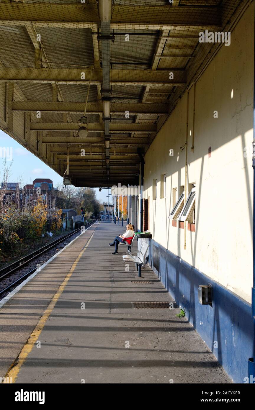 Eine Frau mittleren Alters allein sitzen auf einem leeren Bahnhof Plattform warten auf einen Zug Kingston Station Greater London Surrey England Großbritannien Stockfoto