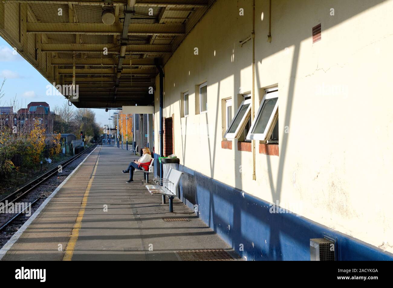Eine Frau mittleren Alters allein sitzen auf einem leeren Bahnhof Plattform warten auf einen Zug Kingston Station Greater London Surrey England Großbritannien Stockfoto